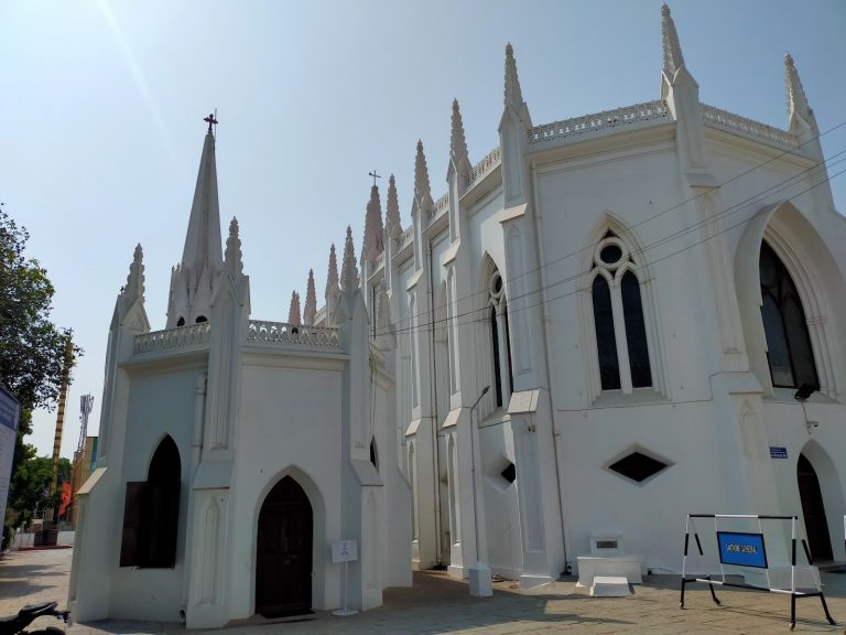 The white neo-Gothic facade and spire of Santhome Cathedral Basilica in Chennai under a clear sky.